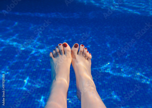 adults woman's feet with red nails underwater in the swimming pool