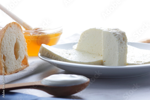 Cheese, honey and sour cream, feta in a white plate, soft cheese on a white background, wooden spoon with sour cream, French breakfast, blue napkin, honey in glassware, blank for designer