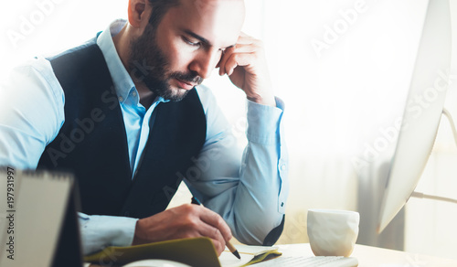 Bearded businessman working on modern office. Consultant man thinking looking in monitor computer. Manager writes in notebook in coworking workplace, startup project concept in studio photo