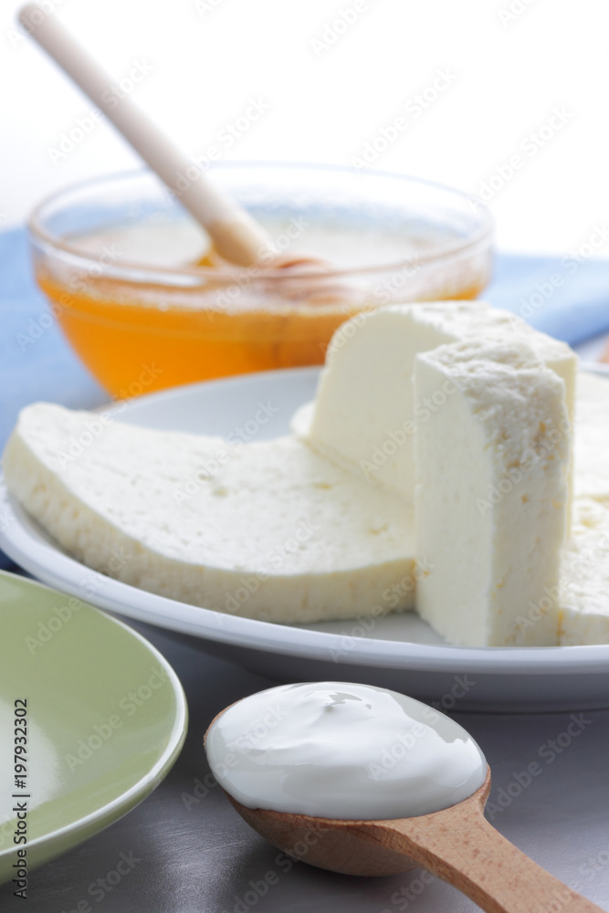 Cheese pattern, honey and sour cream, feta in white and green plate, soft cheese on a white background, wooden spoon with sour cream, French breakfast, blue napkin, honey in glassware Cheese pattern, honey and sour cream, feta in white and green plate, soft cheese on a white background, wooden spoon with sour cream, French breakfast, blue napkin, honey in glassware