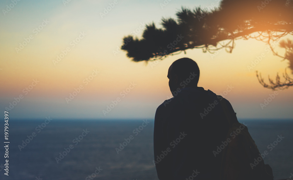 Hipster hiker tourist with backpack looking of amazing seascape sunset on background blue sea, guy enjoying ocean horizon, panoramic sunrise, traveler relax holiday, sunlight view in trip vacation