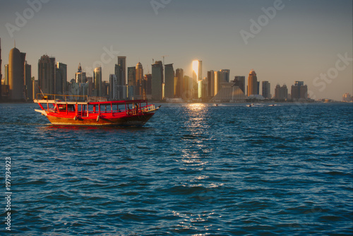 A traditional wooden Dhow cruising with the skyline of West Bay in background, seen at sunset from the Dhow Harbour. Doha, Qatar.