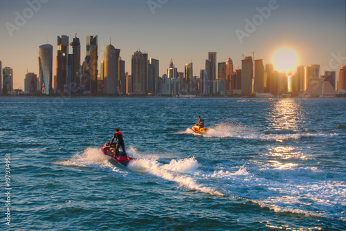 Two jet-skis cruising with the skyline of West Bay in background, seen at sunset from the Dhow Harbour. Doha, Qatar. photo