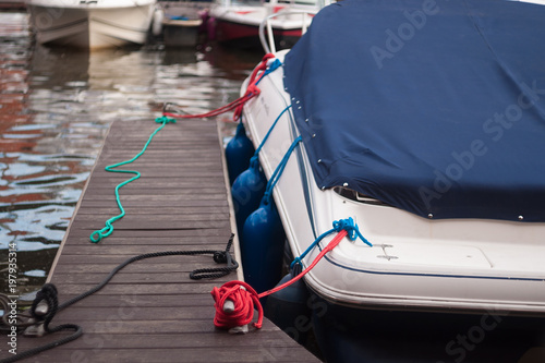 a modern motor boat windshield and bow deck covered in a blue canvas rain cover, with a weathered wood dock and blurry port in background