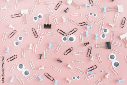 Photos with scattered stationery. Funny faces with puppet eyes and black eyebrows made of paper clips. Stationery buttons, paperclips and asterisks in disorder on a pink background.