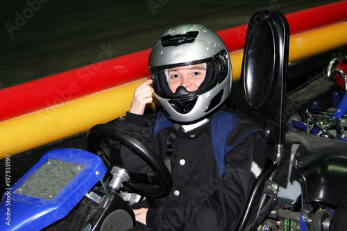 A smiling girl is in a go-kart indoors