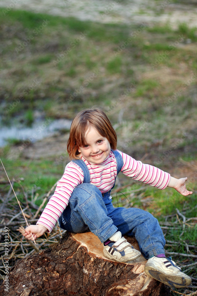 Φωτογραφία A beautiful smiling little girl is sitting on the stump with spreading her arms