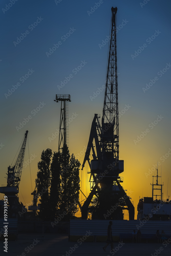 Evening in the port, sea, river dock. Silhouette of industrial cranes. Wharf, Port landscape. Bright sunset