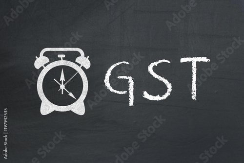 GST concept on blackboard. inscription GST and drawn alarm clock