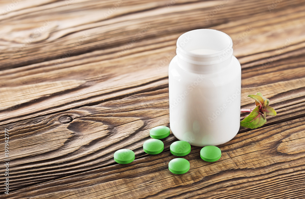 Medical herbal pills in green color and white bottle on wooden background. Concept of herbal healthcare and medicine. Medical herbal pills in green color and white bottle on wooden background. Concept of herbal healthcare and medicine.