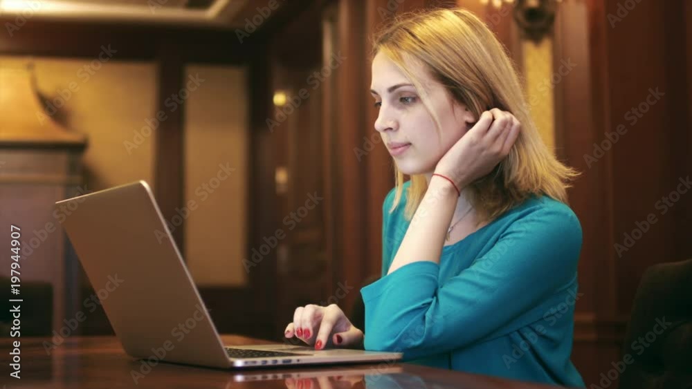 Young woman looking on screen laptop and typing on keyboard. Blonde woman using notebook computer for browsing internet in luxury interior Young woman looking on screen laptop and typing on keyboard. Blonde woman using notebook computer for browsing internet in luxury interior