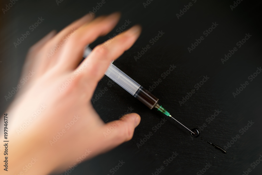 The concept of drug addiction. The hand reaches for the syringe against a dark background. Hand in the effect of movement. The concept of drug addiction. The hand reaches for the syringe against a dark background. Hand in the effect of movement.