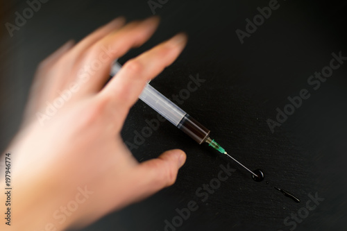 The concept of drug addiction. The hand reaches for the syringe against a dark background. Hand in the effect of movement.