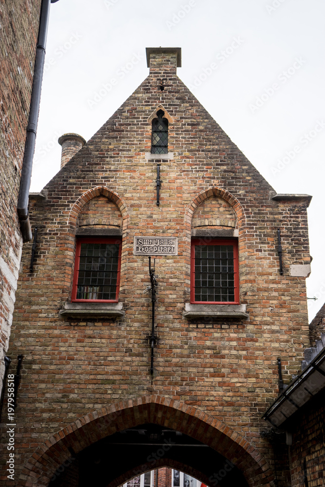 A red brick building with a gable on top an arch in brugge, Belgium