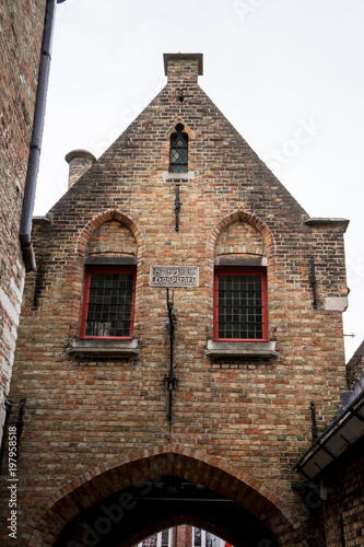 A red brick building with a gable on top an arch in brugge, Belgium © SkandaRamana