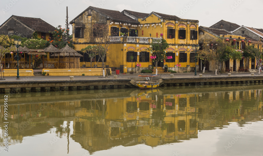 typical mustard yellow buildings with tile roofs reflected on the river in old town of Hoi An, Vietnam 