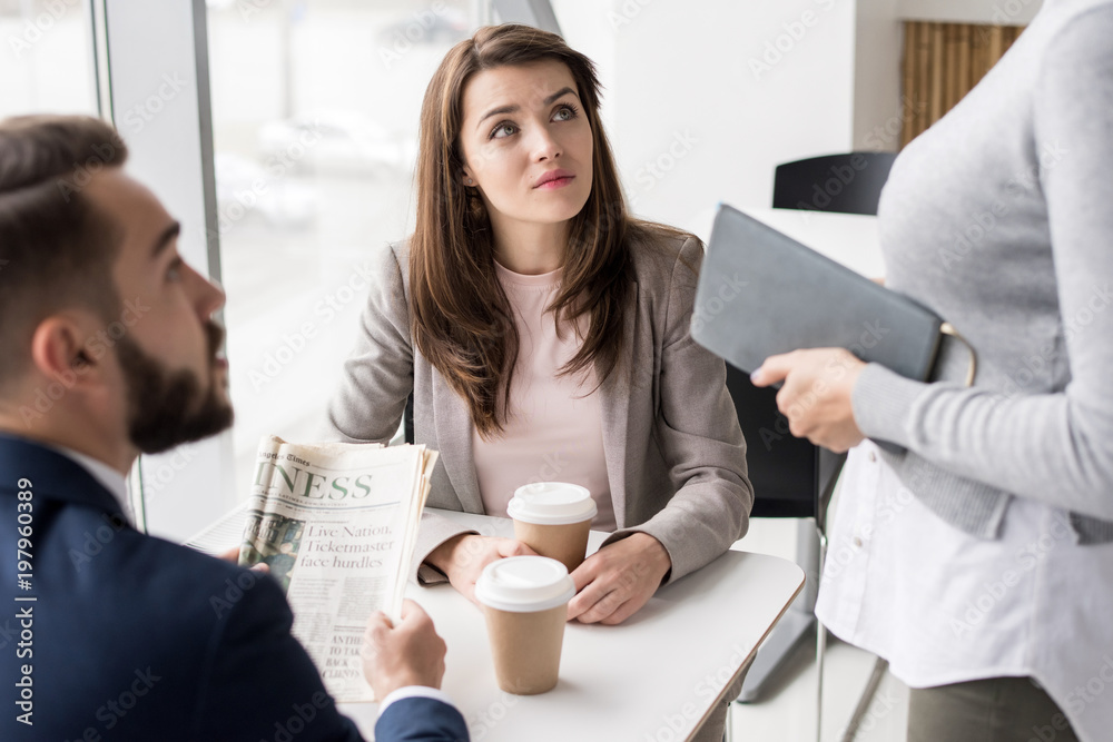 Portrait of three business people discussing work at coffee break in cafe, focus on beautiful young woman looking up