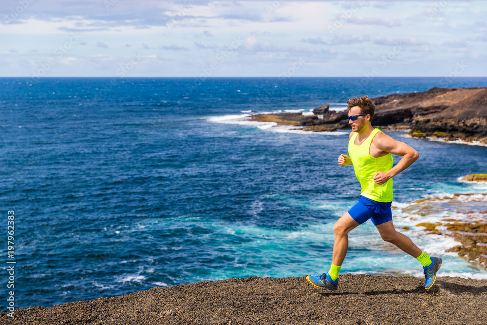 Trail runner athlete man ultra running on rocky trail path with ocean water nature landscape. Active lifestyle of training in nature.