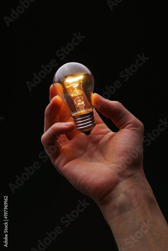 Glowing light bulb in hand on a dark background.