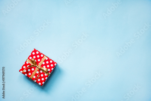 Top view of a red dotted gift box tied with golden bow over blue background. Copy space.