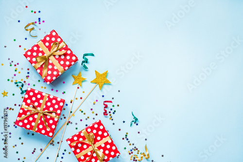 Top view of a red dotted gift boxes, golden magic wands, colorful confetti and ribbons over blue background. Celebration concept. Copy space.