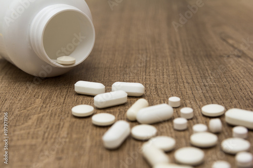 Heap of white capsules on wooden table.