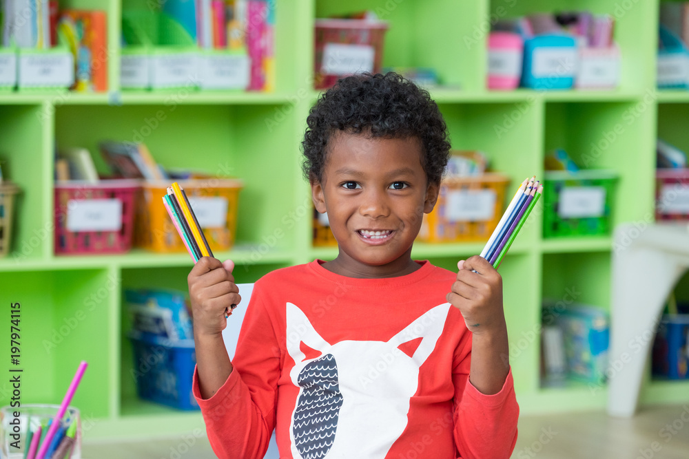 Φωτογραφία African American ethnicity kid holding group of color pencil smiling at library in kindergarten preschool classroom