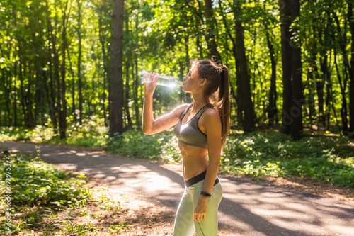 Fitness beautiful woman drinking water and sweating after exercising on summer hot day in park. Female athlete after work out.