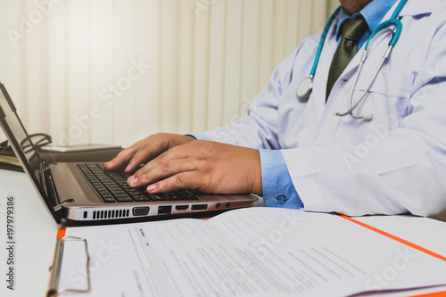 doctor sitting at the table near the window in hospital and typing at laptop computer