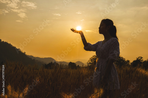 Silhouette of beautiful young woman in barley field white sun on hand.