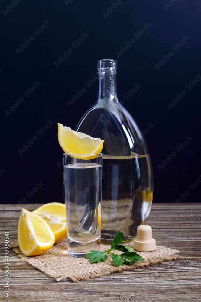 Vodka or tequila in shot glasses and in the bottle with lemon sliсe on rustic wooden background. Traditional strong drink. Close-up. Vertical view Vodka or tequila in shot glasses and in the bottle with lemon sliсe on rustic wooden background. Traditional strong drink. Close-up. Vertical view
