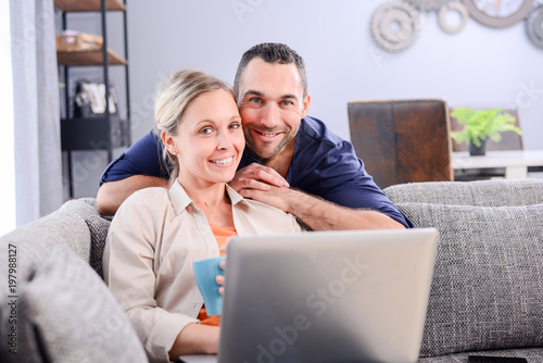 portrait of a young couple relaxed at home in sofa websurfing on internet with laptop computer