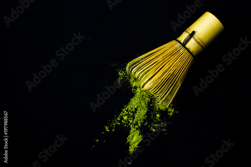 Close up bamboo whisk and matcha green tea powder on black background.