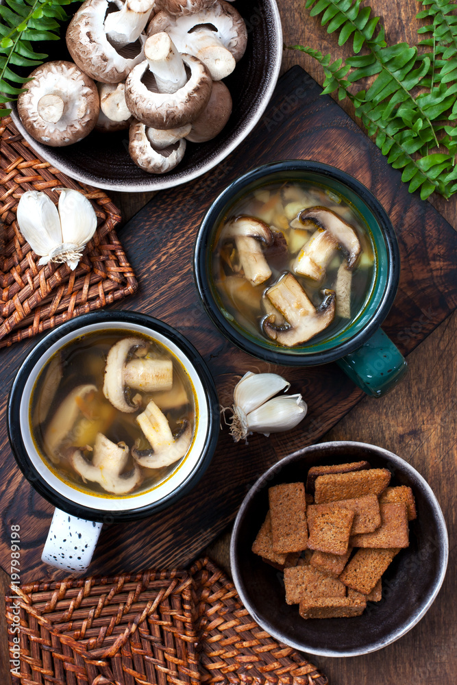 Hot homemade mushroom soup with fried mushrooms in color mug on wooden rustic table and bowl with fresh raw mushrooms Hot homemade mushroom soup with fried mushrooms in color mug on wooden rustic table and bowl with fresh raw mushrooms