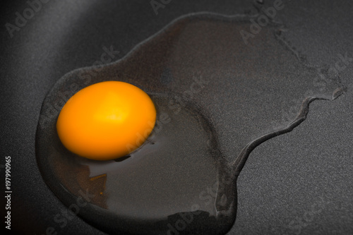 Raw egg on Teflon non-stick frying pan close-up. Kitchen. Black background. Cooking food concept. Yolk and protein of chicken egg. Healthy food. Omelet.