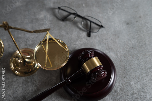 Law and Justice concept. Mallet of the judge, glasses, scales of justice. Gray stone background, reflections on the floor, place for typography. Courtroom theme. © Aerial Mike