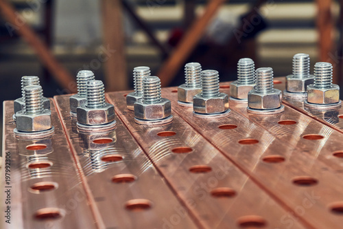 Some flat busbars with holes for fastening of electrical equipment. Metal bolts with nuts and washers are fixed in the holes. Busbars at high current and high voltage. photo