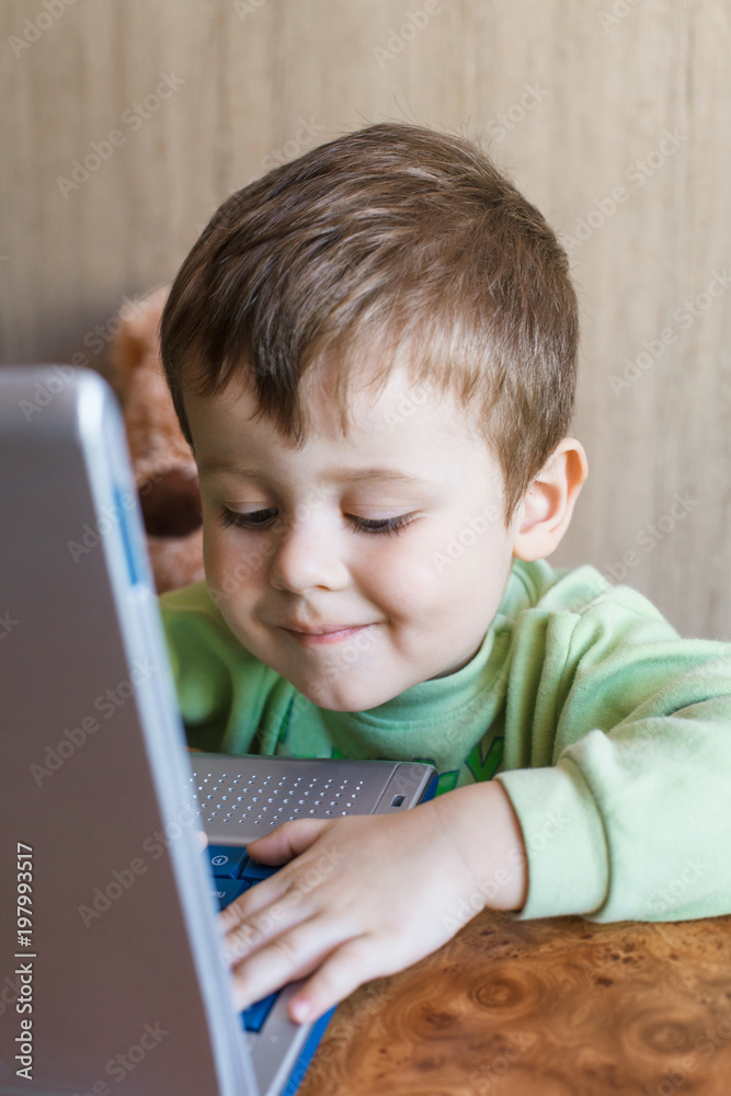 Cute boy is pushing laptops keyboard and he is looking at the screen.