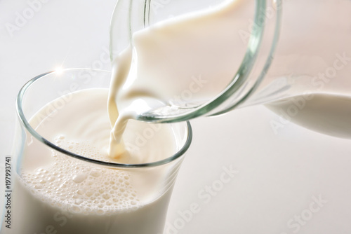 Filling glass of milk with jug on white background