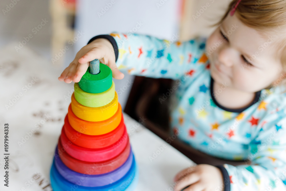 Adorable cute beautiful little baby girl playing with educational wooden rainbow toy pyramid - obrazy, fototapety, plakaty 