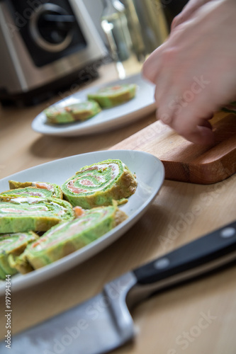 Frau beim Anrichten von Spinat Pfannkuchenrolle mit Räucherlachs und Frischkäse in Küche