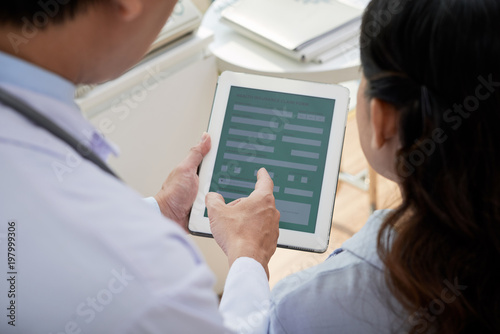 Over shoulder view of male and female physicians gathered together at modern office and using digital tablet while discussing possible treatment for patient