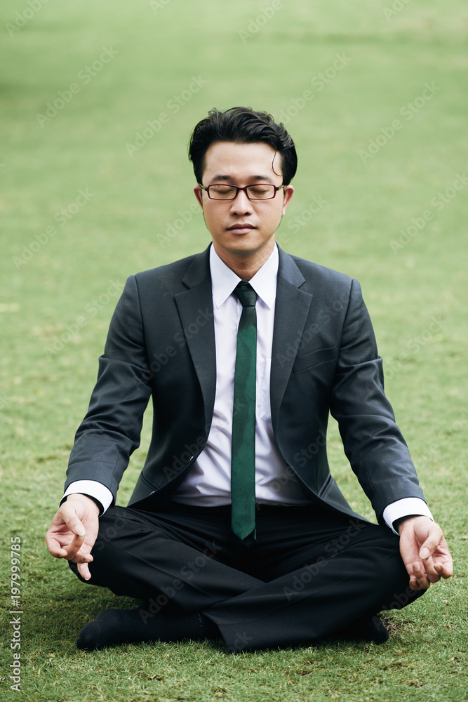 Portrait of Asian businessman in sut meditating on green grass in park Portrait of Asian businessman in sut meditating on green grass in park