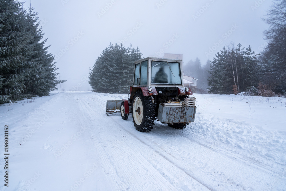 Red snowblower grader clears snow covered ski resort road.
