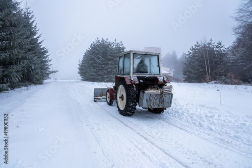 Red snowblower grader clears snow covered ski resort road.