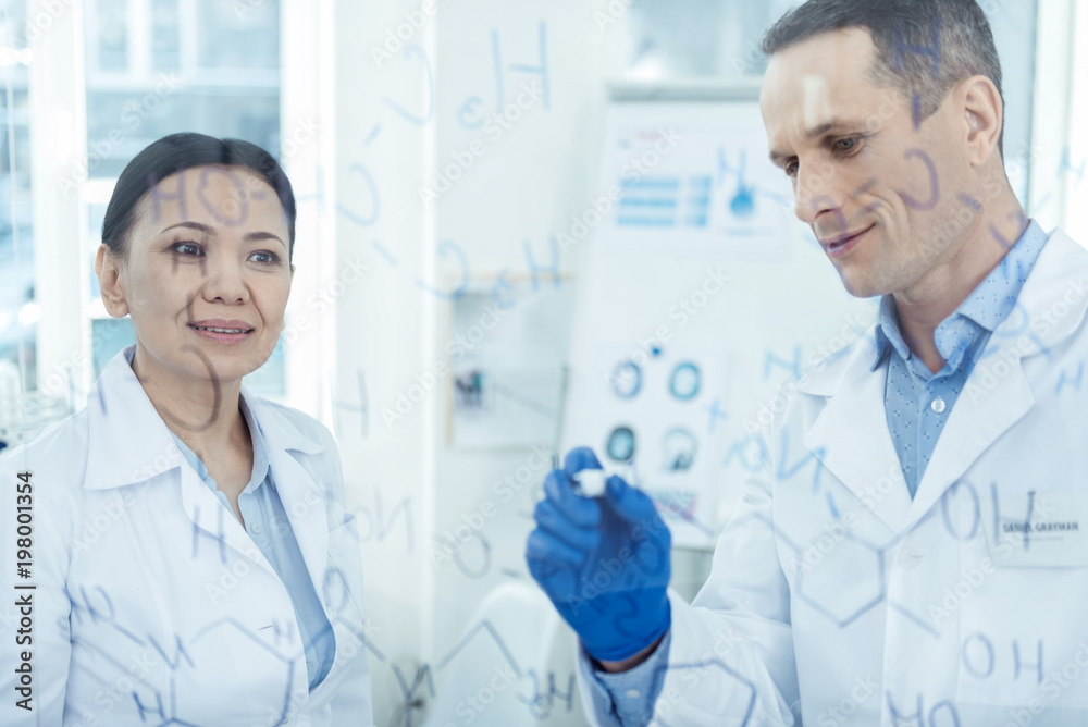 Our project. Attractive delighted smart experienced scientists smiling and writing formulas and discussing their research Our project. Attractive delighted smart experienced scientists smiling and writing formulas and discussing their research