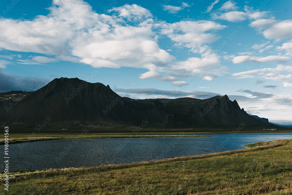 majestic icelandic landscape with calm river between rocky mountains and grassy meadow