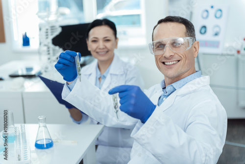 laboratory analysis. Cheerful professional lab workers holding test tubes while conducting a reseacrh