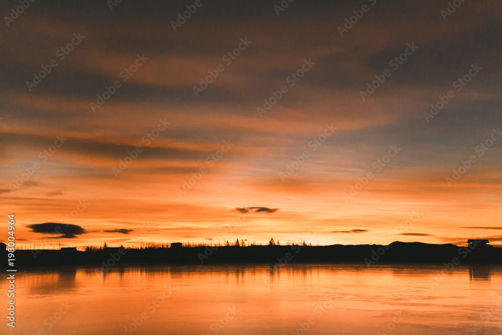 scenic view of skyline with trees and buildings reflected in water at sunset, iceland
