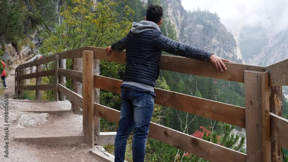 Handsome young man hiking in lush green mountain scenery, walking up the hill, seen from the back then looking at Braies lake or Pragser Wildsee in Trentino region, Italy Handsome young man hiking in lush green mountain scenery, walking up the hill, seen from the back then looking at Braies lake or Pragser Wildsee in Trentino region, Italy